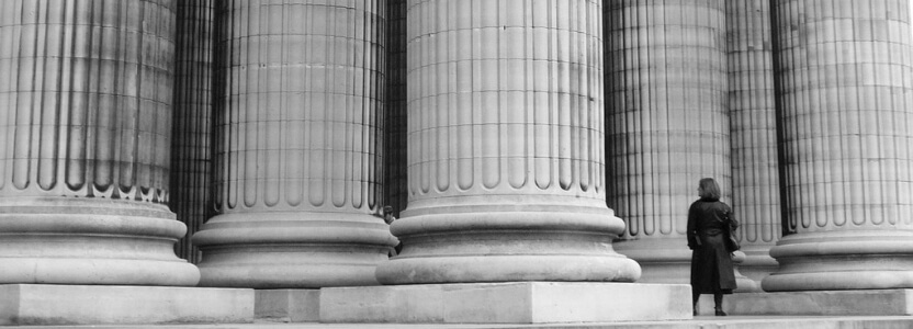 Large white pillars and a woman standing nearby in black and white represent the 3 pillars of motivation that represent characteristics of a leader