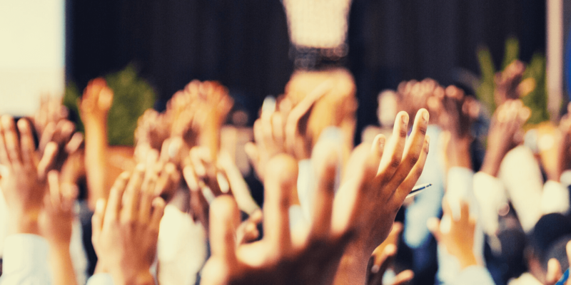 A group of people raising their hands at a seminar indicates the asking of leadership questions